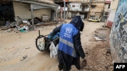 A man collects trash while wearing a jacket bearing the logo of the United Nations Relief and Works Agency for Palestine Refugees in the Near East along a street in the city of Jenin in the occupied West Bank on Jan. 30, 2024.