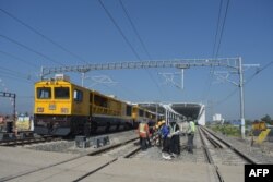 Sebuah kereta api melintas saat para pekerja yang sedang memeriksa sistem elektronik kereta api cepat buatan China yang menghubungkan Ibu Kota Jakarta dengan Bandung, di stasiun Tegalluar, Bandung, Jawa Barat, 15 Mei 2023. (TIMUR MATAHARI/AFP)