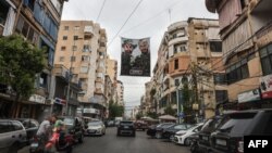 Pengendara mobil melewati poster yang menunjukkan pejuang Hizbullah yang terbunuh di pinggiran selatan Beirut, 21 Juni 2024. (ANWAR AMRO / AFP)