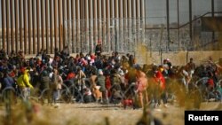 Migrants gather near the border wall after crossing the Rio Bravo river with the intention of turning themselves in to the U.S. Border Patrol agents to request asylum, as seen from Ciudad Juarez, Mexico, Dec. 18, 2023.