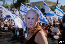 Seorang demonstran yang mengenakan topeng bergambar Perdana Menteri Israel Benjamin Netanyahu ikut serta dalam aksi duduk untuk memblokir pintu masuk Knesset, parlemen Israel, di Yerusalem, 24 Juli 2023. (Foto: AFP)
