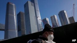 FILE - A migrant worker wearing a face mask walks by construction cranes near the office buildings at the central business district in Beijing, March 15, 2023.