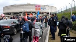Passengers walk with their luggages as airport workers on strike gather outside the Terminal 1 during the ninth day of nationwide strikes and protests against French government's pension reform, at the Paris-Charles de Gaulle airport in Roissy, near Paris, March 23, 2023.
