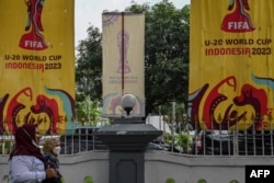 Seorang perempuan melewati spanduk menyambut turnamen sepak bola Piala Dunia FIFA U-20 Indonesia 2023 di Jakarta, 30 Maret 2023. (ADEK BERRY/AFP)