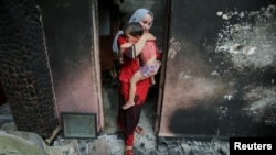Souhila Belkati carries her child inside her burnt house following a wildfire in Bejaia, Algeria, July 25, 2023. 