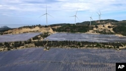 FILE - Solar panels work near wind turbines in Quy Non, Vietnam on June 11, 2023. 
