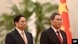 Vietnam's Prime Minister Pham Minh Chinh, left, and Chinese Premier Li Qiang listen to national anthems during a welcome ceremony in the Great Hall of the People in Beijing, June 26, 2023. (Pool photo via AP)