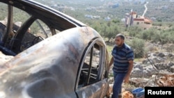 FILE - A Palestinian man checks a car burned in a raid by Israeli settlers near Salfit in the Israeli-occupied West Bank, Dec. 3, 2023.