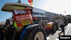 A woman crosses a road next to tractors, as Spanish farmers block access to the Castellon port during a protest against high costs, bureaucracy and competition from non-EU countries, in Castellon, Spain, Feb. 7, 2024.