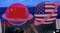 Seorang pedagang menyiapkan makanan dan minuman di stan yang menampilkan planet berbentuk bendera China dan Amerika selama Karnaval Musim Semi di Beijing pada 13 Mei 2023. (Foto: AP)