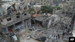 Warga Palestina melihat-lihat di sekitar bangunan yang hancur akibat pengeboman Israel di kamp pengungsi Nuseirat di Jalur Gaza pada Minggu, 29 Oktober 2023. (Foto: AP/Hatem Moussa)