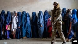 Seorang anggota Taliban berjaga saat kaum perempuan menunggu untuk menerima jatah makanan yang didistribusikan oleh kelompok bantuan kemanusiaan, di Kabul, Afghanistan, 23 Mei 2023. (Foto: AP)