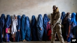 Seorang anggota Taliban berjaga saat perempuan menunggu untuk menerima jatah makanan yang didistribusikan oleh kelompok bantuan kemanusiaan, di Kabul, Afghanistan, 23 Mei 2023. (Foto: AP)