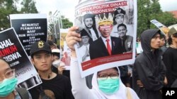 Seorang pengunjuk rasa mengacungkan poster bergambar Presiden Joko Widodo yang dirusak saat aksi protes, menuntut pemilihan presiden yang adil di Yogyakarta, Senin, 12 Februari 2024. (AP/Slamet Riyadi)