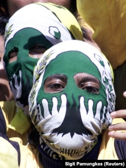 Pendukung Partai Golkar Indonesia menutupi wajah mereka dengan lambang partai pada kampanye di Surabaya, Jawa Timur pada 31 Maret 2004. (Foto: REUTERS/Sigit Pamungkas) ​