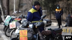 FILE - A migrant worker stands on a street next to signs advertising his work skills as he waits to be hired in Shenyang, in northeastern China's Liaoning province, Feb. 25, 2021.