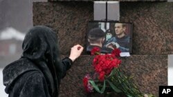 A woman reaches to touch a photo of Alexey Navalny after laying flowers at the Memorial to Victims of Political Repression in St. Petersburg, Russia, Feb. 17, 2024.