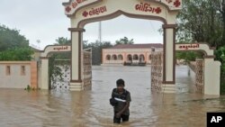 Seorang pria mengarungi jalan yang terendam banjir menyusul angin kencang dan hujan deras setelah topan Biparjoy mendarat di Mandvi di distrik Kutch, negara bagian Gujarat, India Barat, Jumat, 16 Juni 2023. (AP/Ajit Solanki)