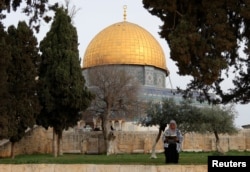 FILE - A Palestinian woman reads the holy book of Koran in the compound known to Muslims as the Noble Sanctuary and to Jews as the Temple Mount, in front of the Dome of the Rock, March 23, 2023.