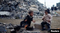Anak-anak Palestina duduk di dekat api di samping puing-puing rumah yang terkena serangan Israel selama konflik, di tengah gencatan senjata sementara antara Hamas dan Israel, di Khan Younis di selatan Jalur Gaza, 27 November 2023. (Foto: reuters )