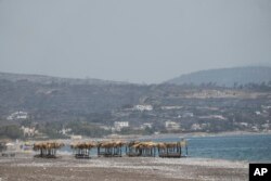 Abandoned sunbeds and umbrellas stand at the beach as a burnt hill is seen in the background after a wildfire, near Gennadi village, on the Aegean Sea island of Rhodes, southeastern Greece, July 27, 2023.