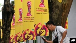 Seorang pria memeriksa ponselnya di dekat spanduk FIFA U-20 World Cup di Jakarta, Kamis, 30 Maret 2023. (Foto: AP)