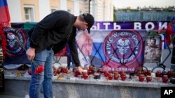 A man puts a candle at a makeshift memorial for Wagner mercenary group members killed in a plane crash last Wednesday, near the Kremlin in Moscow, Aug. 27, 2023. Listed among the dead was Yevgeniy Prigozhin, the group's leader (pictured to the left of the Wagner emblem).