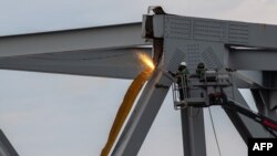 This handout photo obtained from the US Coast Guard on March 31, 2024 shows demolition crews cutting the top portion of the north side of the collapsed Francis Scott Key Bridge into smaller sections, in Baltimore, March 30, 2024.