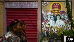 两名维吾尔妇女从喀什街道树立的政府宣传画前走过。（2023年7月14日）