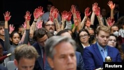 Para pengunjuk rasa antiperang mengangkat tangan "berdarah" dan tulisan "Free Gaza" di belakang Menlu AS Antony Blinken saat sidang Komisi Senat membahas bantuan bagi Israel dan Ukraina di Gedung Capitol, Washington DC, 31 Oktober 2023.