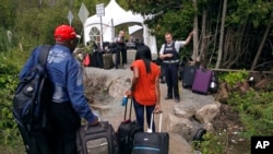 FILE - A Royal Canadian Mounted Police officer informs a migrant couple of the location of a legal border station, shortly before they illegally crossed from Champlain, New York, to Saint-Bernard-de-Lacolle, Quebec, using Roxham Road, Aug. 7, 2017.