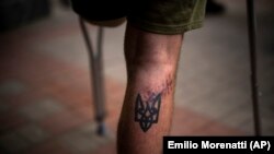 资料照 - 照片上一名乌克兰亚速营伤员受伤的小腿上纹着亚速营标志的刺青。照片摄于2022年5月5日，这位伤员拄着拐杖去基辅一家医院参加康复锻炼。