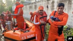 In this photo made available by the National Disaster Response Force (NDRF) on Aug. 15, 2023, an NDRF personnel carries an infant to safety in flood-affected Himachal Pradesh state, India. 