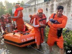 Seorang anggota Pasukan Tanggap Bencana Nasional India (NDRF) menggendong bayi ke tempat yang aman di wilayah negara bagian Himachal Pradesh yang dilanda banjir, Selasa, 15 Agustus 2023. (Foto: NDRF via AP)