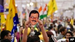 Seorang pendukung Partai Aam Admi memegang topeng yang mirip dengan pemimpin partai dan Ketua Menteri Delhi Arvind Kejriwal saat berdemonstrasi di New Delhi, India, Minggu, 31 Maret. 2024. (Foto: AP)