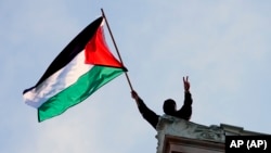 Seorang mahasiswa mengibarkan bendera Palestina di atas Hamilton Hall di kampus Universitas Columbia, pada 30 April 2024. (Foto: Pool Foto/Mary Altafer)
