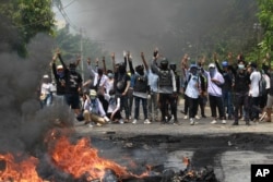 FILE - Anti-coup protesters gesture with a three-fingers salute, a symbol of resistance to the military junta, during a police crackdown in Thaketa township, Yangon, Myanmar, March 27, 2021.