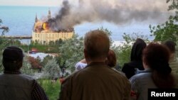 29일 러시아 군의 집속탄 공격으로 파괴된 우크라이나 대학 건물을 시민들이 바라보고 있다.