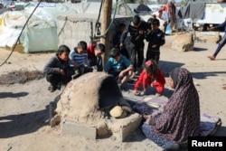 Seorang perempuan Palestina membuat roti sementara anak-anak duduk di sebelahnya. Penduduk Gaza menghadapi krisis kelaparan dan meningkatnya kekurangan gizi, di Khan Younis di Jalur Gaza selatan, 24 Januari 2024. (Foto: Reuters)