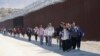 FILE - A group of people, including many from China, walk along the wall after crossing the border with Mexico to seek asylum, near Jacumba, California, Oct. 24, 2023.