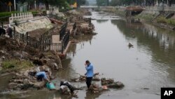 Residents wash their suitcase and belongings on a damaged bank of a canal clogged with flood debris in the aftermath of river flooding in the Mentougou district on the outskirts of Beijing, Aug. 7, 2023.