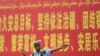 Seorang polisi tampak berdiri di depan papan iklan propaganda yang berbunyi "pemeliharaan aturan hukum di Xinjiang" yang ditulis dalam Bahasa Mandarin dan Uyghur dan terpasang di sebuah jalan di prefektur Kashgar, Xinjiang, pada 19 Juli 2023. (Foto: AFP/Pedro Pardo)