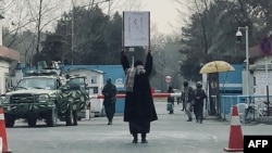 Seorang mahasiswi melakukan aksi protes seorang diri, menentang larangan pendidikan tinggi bagi perempuan, di hadapan para anggota Taliban yang berjaga di luar Universitas Kabul, 25 Desember 2022. (AFP)