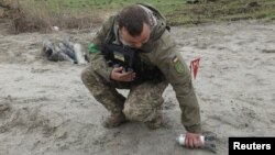 Seorang tentara pencari ranjau tampak mengambil serpihan bom tandan yang gagal meledak di area dekat desa Motyzhyn, di Kyiv, Ukraina, pada 10 April 2022. (Foto: Reuters/Mykola Tymchenko)