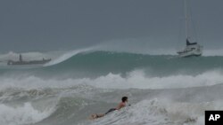 Seorang peselancar tampak mengarungi ombak di Teluk Carlisle di saat badai Beryl melewati wilayah Bridgetown, Barbados, pada 1 Juli 2024. (Foto: AP/Ricardo Mazalan)