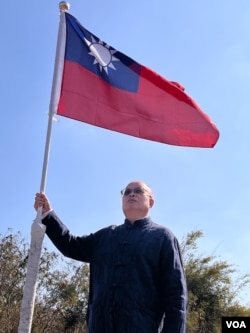 Retired army colonel Honor Ni stands next to a flag in his front yard, Jan. 16, 2024. (Elizabeth Lee/VOA)