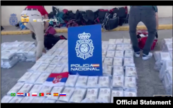 Fotografija napravljena od video snimka koji je objavio MUP Srbije 1. septembra 2023, na kojoj se vide zaplenjeni paketi kokaina ispod pločice sa grbom španske policije i zastave Republike Srbije, na brodu u Atlantiku.