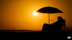 Arhiva - Čovek se odmara ispod suncobrana tokom zalaska Sunca, u Njuport Biču, Kalifornija.
