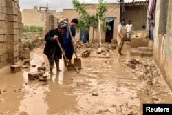 People remove mud from the courtyard of their houses after floods in Maymana, the capital city of Faryab province, Afghanistan, May 19, 2024.