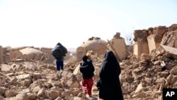 Seorang perempuan Afghanistan bersama anaknya berjalan melewati reruntuhan bangunan pasca gempa yang melanda provinsi Herat, Afghanistan, pada 15 Oktober 2023. (Foto: Save the Children via AP)